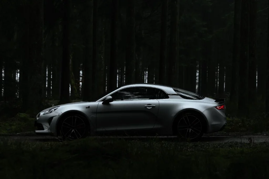 An Alpine sports car photographed at dusk on a forest road.
