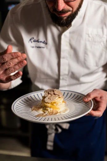A chef in a white jacket presenting a plated dish for a food shoot.