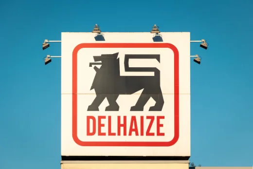 The Delhaize lion sign on a storefront against a blue sky.